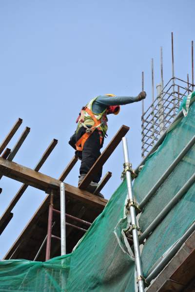 Bauarbeiter steht auf wackligen Brettern auf Baustelle in großer Höhe und blickt nach unten