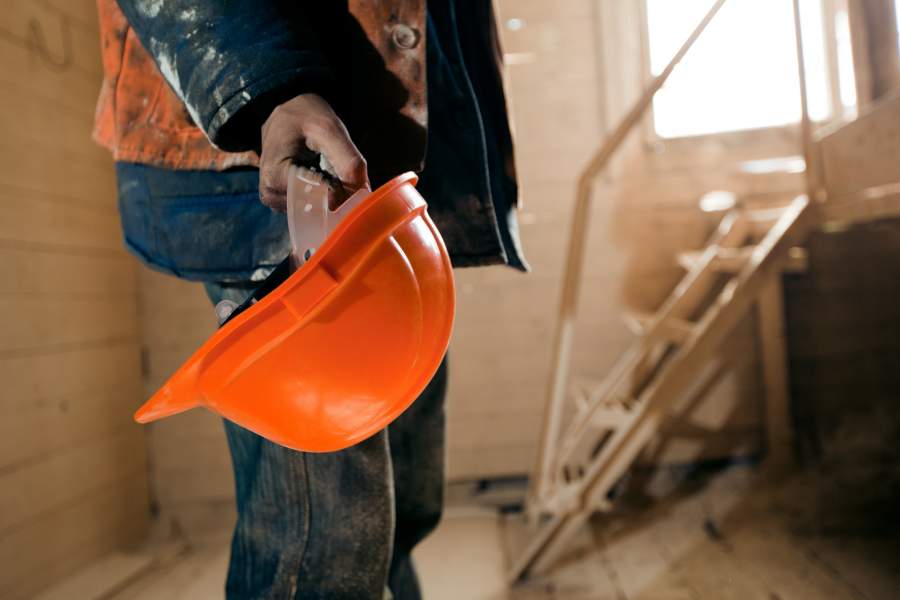 Handwerker hält einen neuen orange-farbenen Schutzhelm in der Hand auf der Baustelle